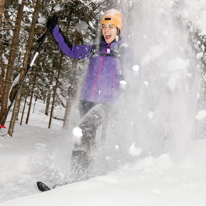 Snow falling from a tree onto a woman wearing snowshoes