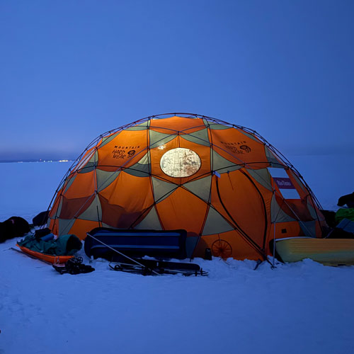 Vue extérieure, en soirée, d’une tente installée sur le lac Saint‑Jean. 